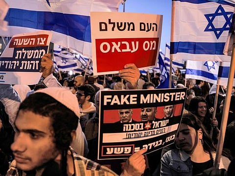 A demonstrator holds up a sign reading in Hebrew "the people pay the Abbas tax" (behind), while another shows a sign showing the faces of (L to R) Israeli Foreign Minister and alternate prime minister Yair Lapid, Israeli conservative Islamic party Raam leader Mansour Abbas, and Prime Minister Naftali Bennett, with text in English reading "Fake Minister" and in Hebrew "Israel is in danger, we want a Jewish state", during an anti-government protest by Israeli right-wing supporters in Jerusalem on April 6, 2022.