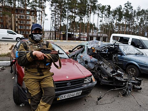 A member of the Ukrainian Territorial Defence Forces sits next to a destroyed car, amid Russia's attack on Ukraine, in Irpin, Kyiv region, Ukraine April 18, 2022.