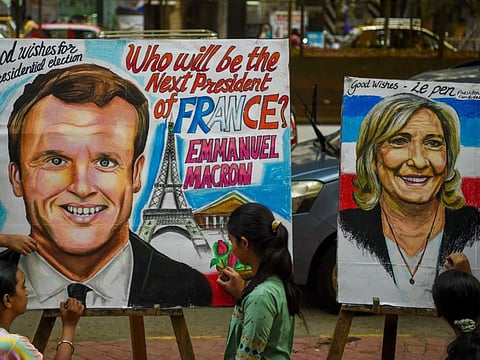 Students pose near paintings of French President and liberal party La Republique en Marche (LREM) candidate for re-election Emmanuel Macron and French far-right party Rassemblement National (RN) presidential candidate Marine Le Pen ahead of the second round of the French presidential election, at an art school in Mumbai on April 19, 2022.
