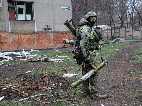 An armed serviceman of Donetsk People's Republic militia walks past a building damaged during fighting in Mariupol.