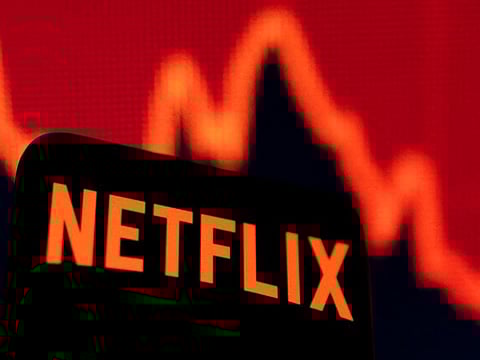 Smartphone with Netflix logo is seen in front of a descending stock graph