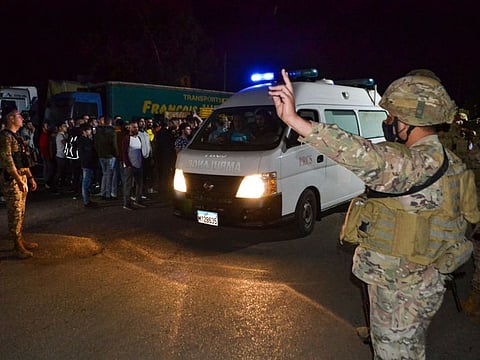 Lebanese soldiers and onlookers stand at the entrance of the port of Tripoli, as an ambulaNce carrying survivors from a boat that sank off the coast of the northern city, leaves during the night of April 23, 2022