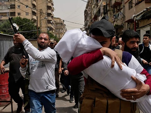 A man carries the body of a young girl, as a mourner fires in the air during the funeral procession for seven people killed when a boat packed with migrants sank over the weekend as the Lebanese navy tried to force it back to shore, in Tripoli, north Lebanon, on April 25, 2022.