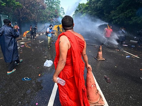 A Buddhist monk looks on as police use tear gas and water cannon to disperse university students protesting to demand the resignation of Sri Lanka's President Gotabaya Rajapaksa over the country's crippling economic crisis, near the parliament building in Colombo on May 6, 2022.