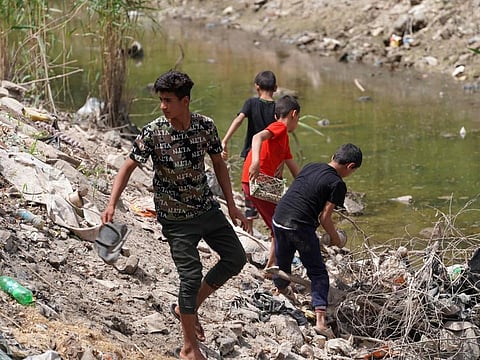 Iraqi youths gather on th banks of a drying and polluted stream, in Iraq's central province of Najaf, on May 1, 2022.