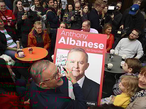 Australia's Prime Minister-elect Anthony Albanese, centre, signs a poster for twin brothers Dimitri and Stavros, bottom right, as he visits a coffee shop in suburban Marrickville, Sydney, May 22, 2022.