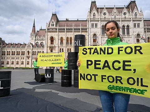 An activist of independent global campaigning network Greenpeace holds a banner reading 'Stand for peace not for oil' in front of the parliament building in Budapest, Hungary on May 30, 2022, to demand from the Hungarian government not to oppose EU sanctions on Russian oil.