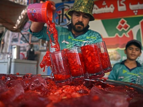A vendor prepares to serve Rooh Afza watermelon beverages to customers along a roadside stall in Karachi.