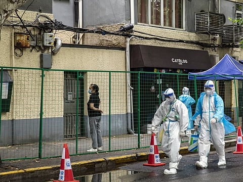 Workers in personal protective equipment (PPE) pass a fence surrounding a neighborhood placed under lockdown due to Covid-19 in Shanghai, China, on Friday, June 10, 2022.