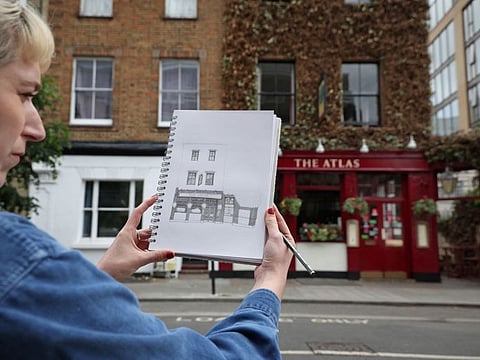 Artist Lydia Wood holds up her partially finished drawing of The Atlas pub in west London on May 26, 2022. - The 28-year-old artist has built up a TikTok and Instagram following with her detailed sketches of well-loved London pubs and has set an ambitious -- but she thinks, not impossible -- goal of drawing all 3,500 of them. )