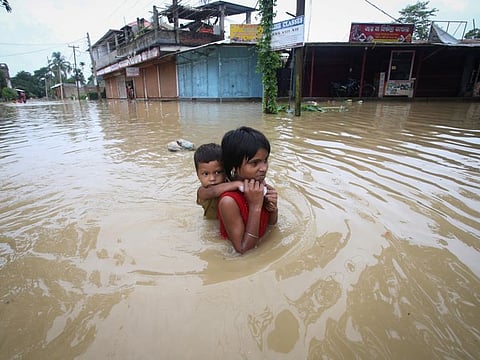 A girl carries her brother as she wades through a flooded road after heavy rains, on the outskirts of Agartala, India, on June 18, 2022.