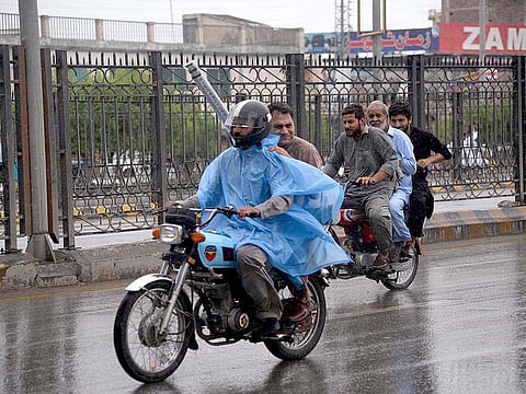 Motorcyclists cover up with polythene sheet during rain in the Peshawar.