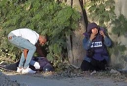 This file image grab taken from footage distributed by Al Jazeera TV on May 11 shows a reporter reacting (right) as an unidentified man tries to lift the body of the channel's veteran journalist Shireen Abu Akleh from the ground after she was fatally wounded by gunfire in Jenin in the occupied West Bank.