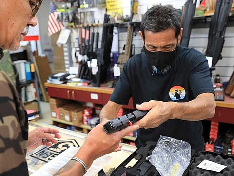 A clerk hands a gun to a customer inside a gun shop, Thursday, June, 23, 2022 in Honolulu.