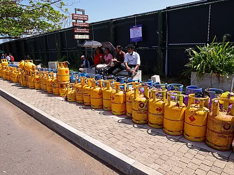 People sit by the lines of empty cooking gas cylinders surrounding the Galle International Cricket Stadium in Galle, Sri Lanka, on Tuesday, June 28, 2022.