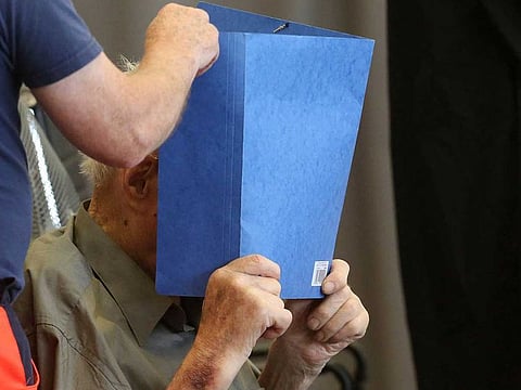 Former Nazi concentration camp guard Josef Schuetz (R) hides his face with a folder as he arrives on June 28, 2022 at a gym used as a makeshift courtroom in Brandenburg an der Havel, eastern Germany, where his verdict was spoken.