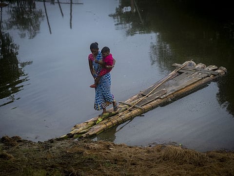 A woman carrying her child walks on a makeshift banana raft after crossing a flooded area at a village in Morigaon district, east Gauhati, Assam state, India, Tuesday, June 28, 2022.