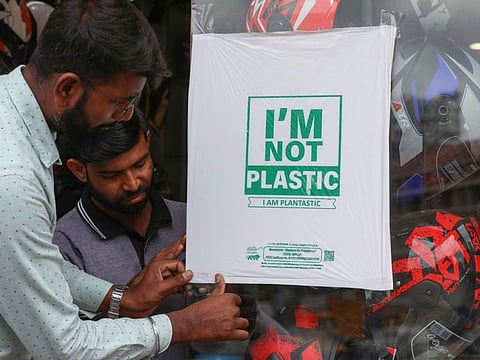Workers of a helmet store paste degradable plastic substitute material on a glass in Hyderabad, India, Thursday, June 30, 2022.
