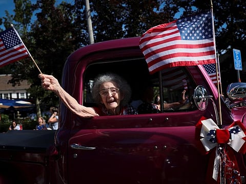 96-year-old Mabel Wittenmeyer waves an American flag as she rides in an antique car during the annual fourth of July parade in Barnstable Village, on Cape Cod, Massachusetts, on July 4, 2022.