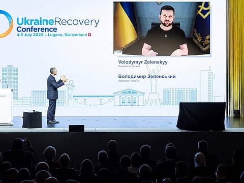 Swiss President Ignazio Cassis (left) introduces Ukrainian President Volodymyr Zelensky (giant screen) prior to his address at the start of a two-day International conference on reconstruction of Ukraine, in Lugano on July 4, 2022.