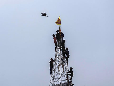 Sri Lankans climb atop a makeshift scaffolding to hoist the national flag near the site of a nationwide protest in Colombo, on July 11, 2022.