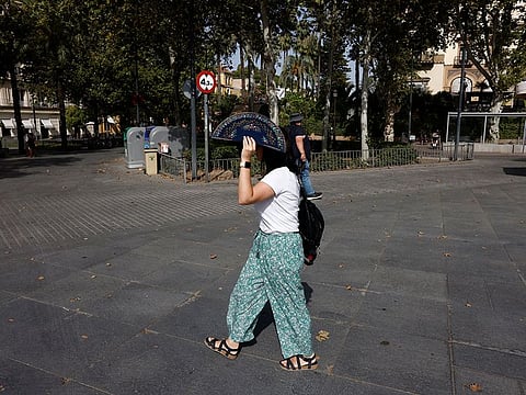 A woman uses a fan to cover her head from the sun as she walks in a street during the second heatwave of the year, in Seville, southern Spain.