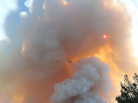 A picture taken on July 13, 2022 shows a firefighting helicopter flying over a wildfire forest which fire broke out in the Datça district of Mugla, Turkey.