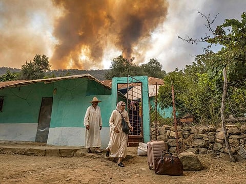 People evacuate a house as a wild forest fire rages in Morocco's northern region of Ksar Sghir on July 14, 2022.