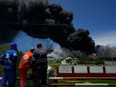 Workers of the Cuba Oil Union, known by the Spanish acronym CUPET, watch a huge rising plume of smoke from the Matanzas Supertanker Base, as firefighters work to quell a blaze which began during a thunderstorm the night before, in Matazanas, Cubao on Aug. 6, 2022.