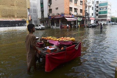 A fruit vendor pushes his cart across a flooded street following heavy monsoon rains in Karachi on July 26, 2022.