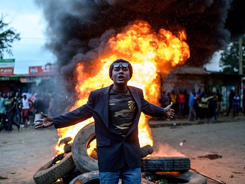 A supporter of Kenya's Azimio La Umoja Party (One Kenya Coalition Party) presidential candidate Raila Odinga gestures past a fire during a protest against the results of Kenya's general election in Kibera, Nairobi, western Kenya.