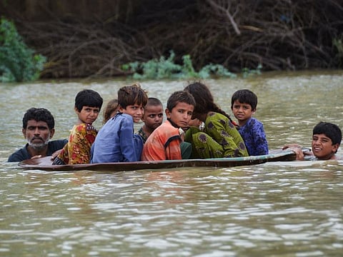 A man (L) along with a youth use a satellite dish to move children across a flooded area after heavy monsoon rainfalls in Jaffarabad district, Balochistan province, on August 26, 2022.