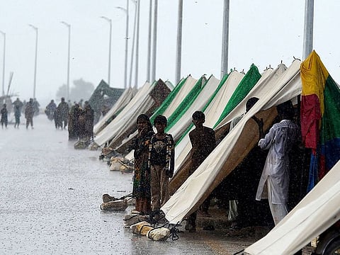 People who fled their flood hit homes stand outside temporary tents set along a road during a heavy rainfall in Sukkur, Pakistan