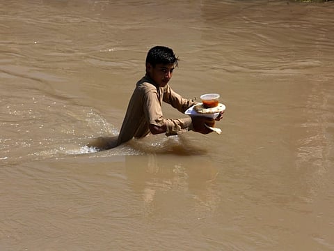 A displaced boy who fled his flood-hit home carries food rations as he wades through a flooded area on the outskirts of Peshawar, on August 28, 2022.