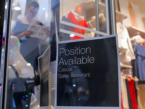 A sales assistant is seen through the window of a retail store displaying a job vacancy sign in central Sydney.