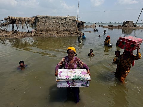 Women carry belongings salvaged from their flooded home after monsoon rains, in the Qambar Shahdadkot district of Sindh Province, of Pakistan, Tuesday, Sept. 6, 2022. More than 1,300 people have been killed and millions have lost their homes in flooding caused by unusually heavy monsoon rains in Pakistan this year that many experts have blamed on climate change. (AP Photo/Fareed Khan)