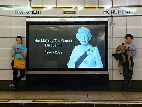 London Underground train passengers wait on a platform beside a billboard image of Britain's Queen Elizabeth, following her death on September 10, 2022.