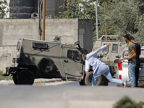 A Palestinian hurls a stone at an Israeli army vehicle during clashes after Israeli forces killed Palestinian gunmen in a raid, in Jenin in West Bank on September 28, 2022.