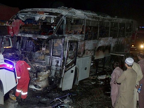 Volunteers gather beside a charred bus on a highway in Nooriabad, Pakistan, on Oct. 13, 2022.