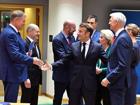 French President Emmanuel Macron, centre, greets Romania's President Klaus Werner Ioannis, left, during a round table meeting at an EU summit in Brussels, on Oct. 21, 2022.