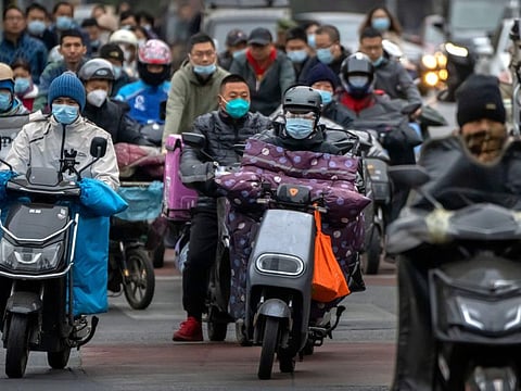 Commuters ride scooters along a street in the central business district in Beijing, on October 28, 2022.