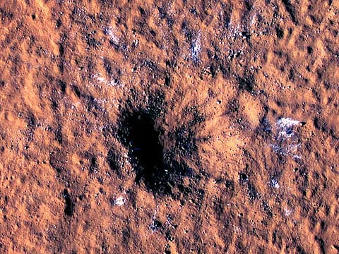 Boulder-size blocks of water ice are seen around the rim of an impact crater on Mars, as viewed by the High-Resolution Imaging Science Experiment (HiRISE camera) aboard NASA's Mars Reconnaissance Orbiter.