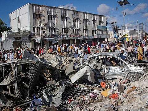 People walk amidst destruction at the scene, a day after a double car bomb attack at a busy junction in Mogadishu, Somalia Sunday, Oct. 30, 2022.