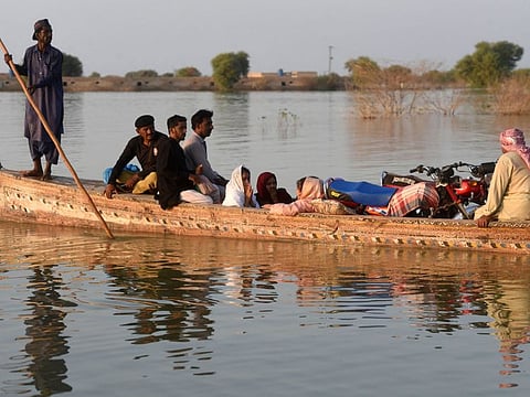 Internally displaced people use a boat to cross a flooded area at Dadu in Sindh province on October 27, 2022.