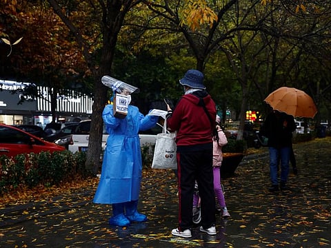 A worker guides people to scan health QR code at a nucleic acid test booth for the COVID-19, in Beijing, on November 11, 2022.