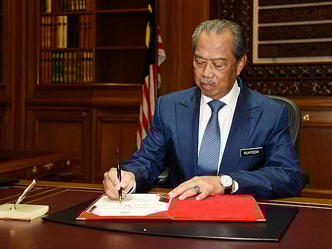 This handout file photo taken and released on March 2, 2020 by Malaysia's Department of Information shows Muhyiddin Yassin signing a document on his first day of work as Malaysia's then-prime minister after he was sworn in following the reformist government's collapse, in Putrajaya.