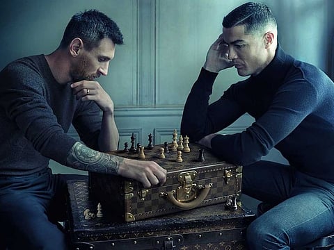 The two great rivals, Messi and Ronaldo, face off over a chessboard improvised from a Louis Vuitton Damier attaché case.