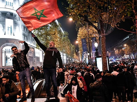 Morocco's supporters wave a national flag to celebrate their national team's victory after the Qatar 2022 World Cup football match between Morocco and Spain, on the Champs Elysees in Paris.