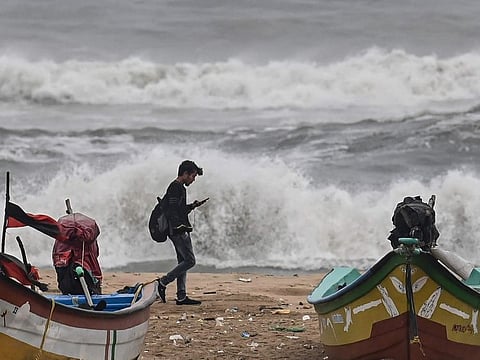 A man walks past fishing boats along a beach amid high winds in Chennai on December 8, 2022, ahead of Cyclone Mandous.