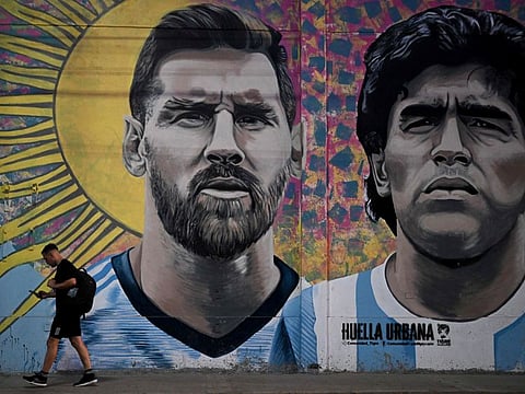 A man passes by a mural depicting Argentine football stars Lionel Messi (left) and late Diego Maradona ahead of the Qatar 2022 World Cup final between Argentina and France in Buenos Aires.